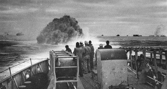 Sailors on a ship's deck watching an explosion in the sea