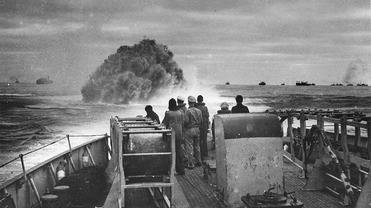 Sailors on a ship's deck watching an explosion in the sea